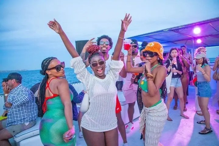 Group of people dancing and smiling on a boat party, with colorful attire and a sunny backdrop.