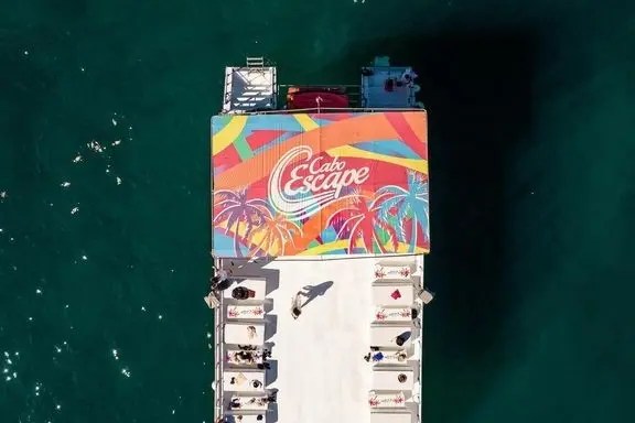 Aerial view of a boat with colorful canopy and people swimming nearby in the ocean.