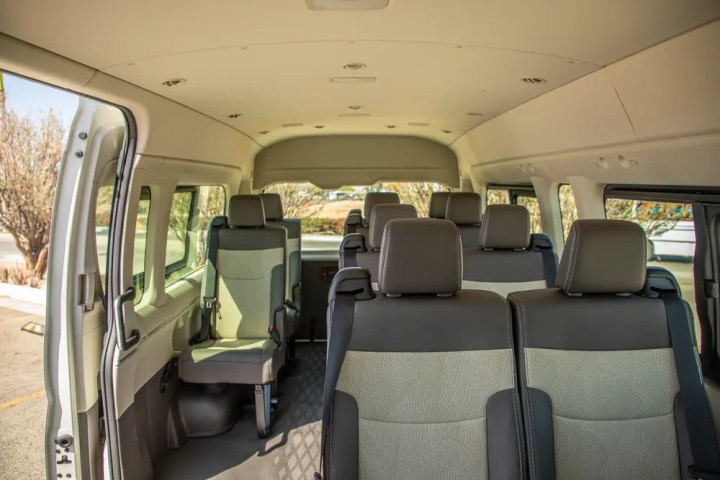 Interior of an empty passenger van with three rows of seats and windows on the sides.